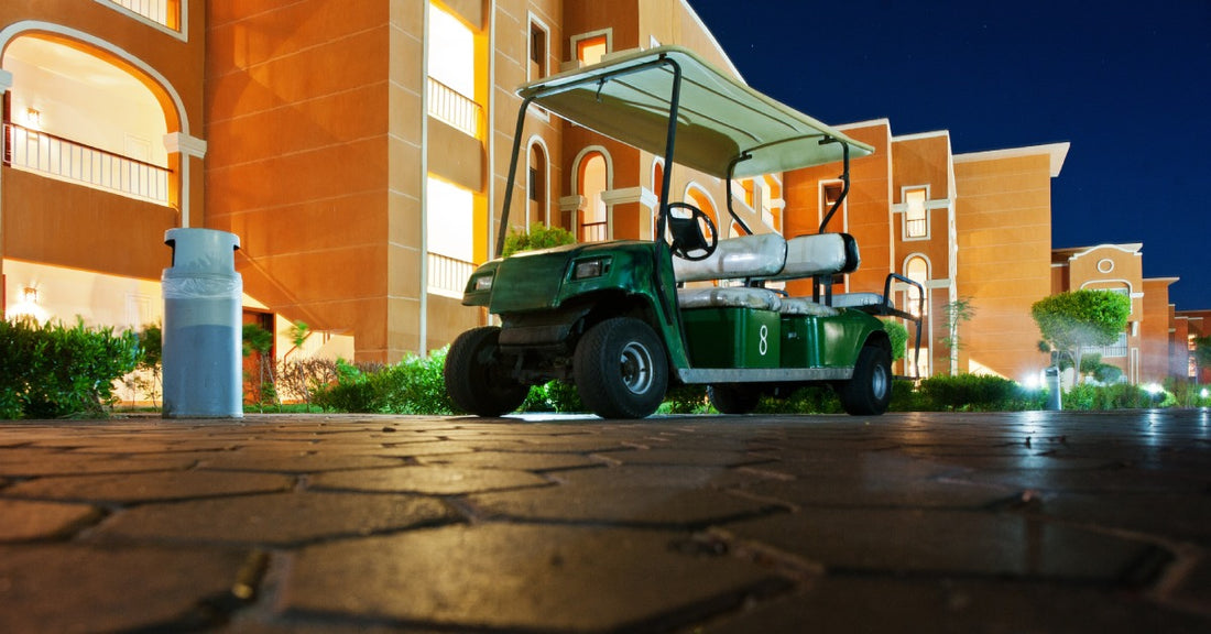 A green, three-row golf cart parked on a hexagon-brick pathway in front of a resort building at night.